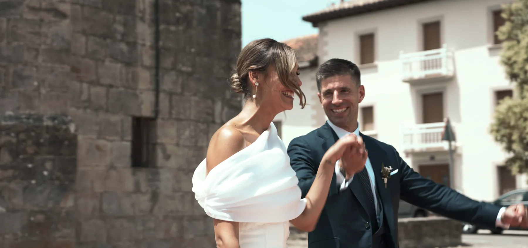 Fotograma de vídeo de boda de DOME Weddings: los novios ríen frente a un edificio blanco