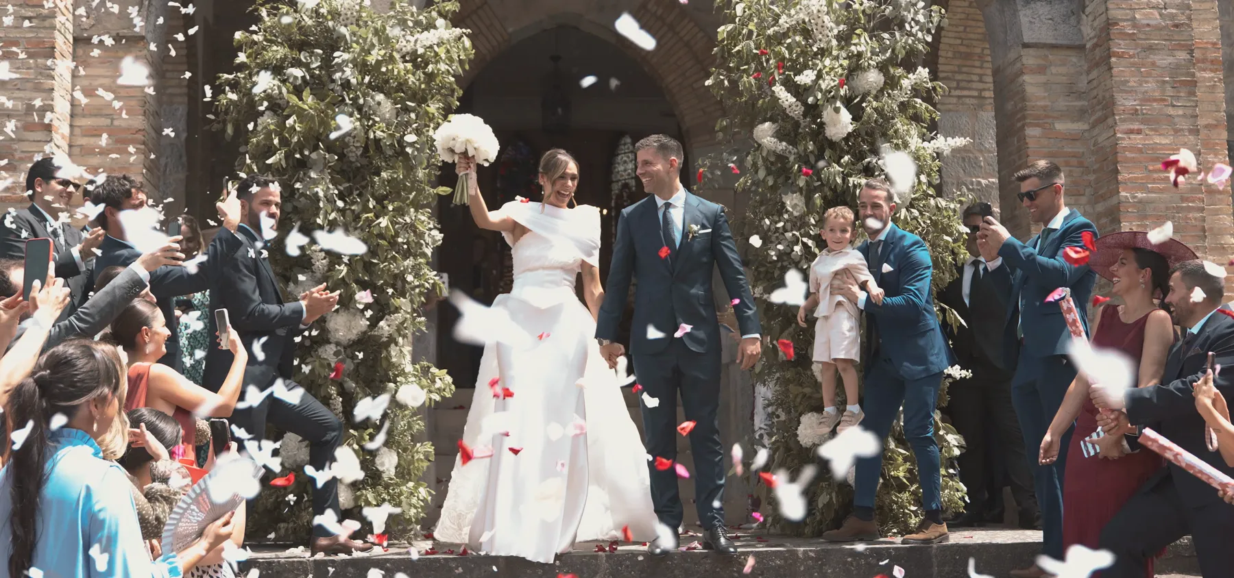 Fotograma de vídeo de boda de DOME Weddings: los novios salen de la iglesia entre pétalos